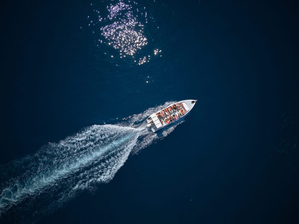 Luftaufnahme eines Motorboots mit Passagieren, das eine weisse Kielwasserspur durch das tiefblaue Meer zieht.