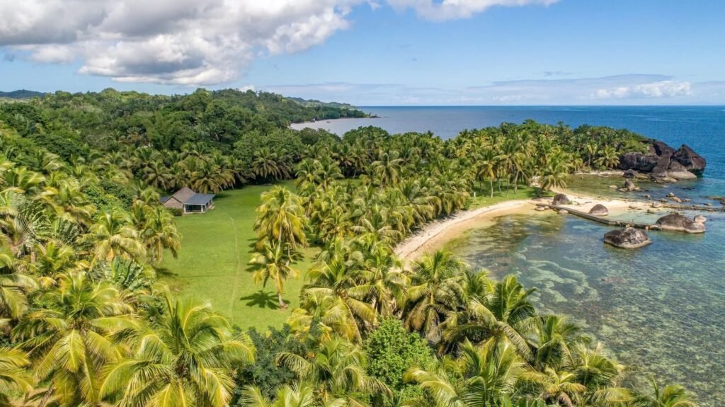 Luftaufnahme der Coco Bay auf Sainte Marie mit Palmenhain, hellem Sandstrand, Granitfelsen und türkisfarbenem Wasser.