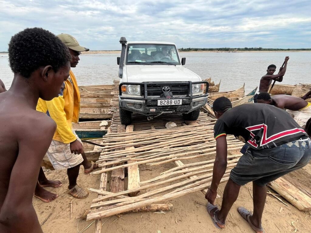 Geländewagen auf einer Flussfähre bei Bevoay in Madagaskar, während Männer die hölzerne Auffahrrampe ausrichten.