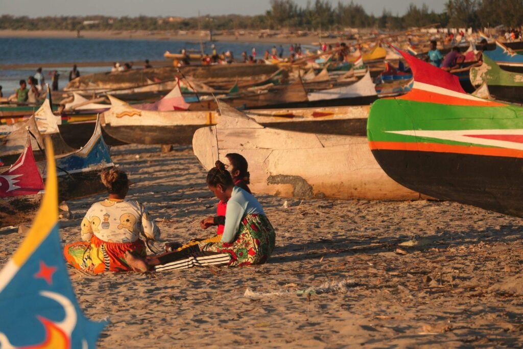 Menschen zwischen bunten Fischerbooten am Strand von Morombe in Madagaskar im warmen Abendlicht.