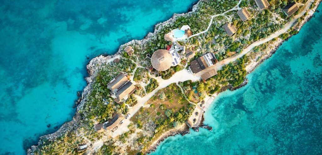 Luftaufnahme der Olô Bé Lodge mit Bungalows und Pool auf einer felsigen Landzunge, umgeben von türkisfarbenem Meer.