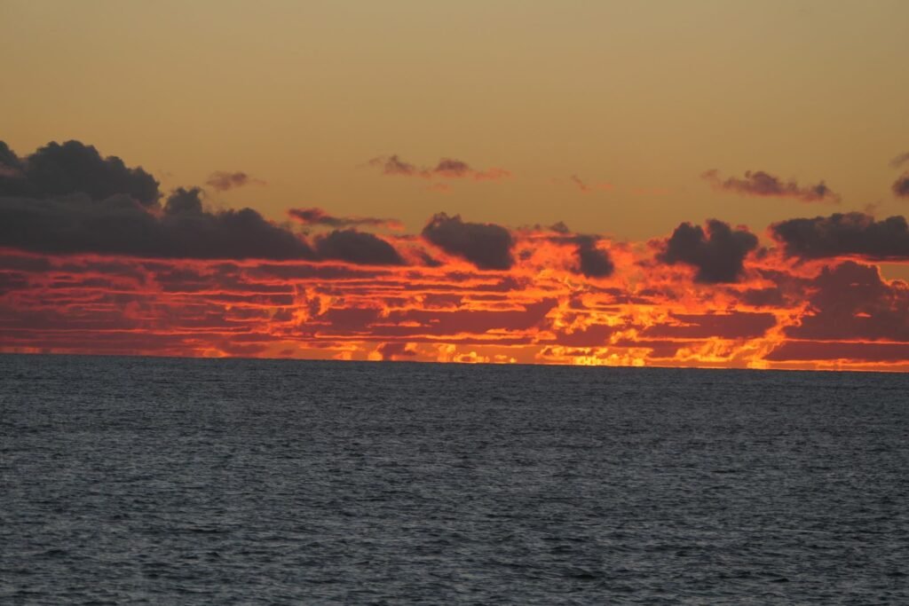 Sonnenuntergang über dem Meer bei Saint Augustin in Madagaskar mit leuchtend orangefarbenem Himmel und dunklen Wolken.